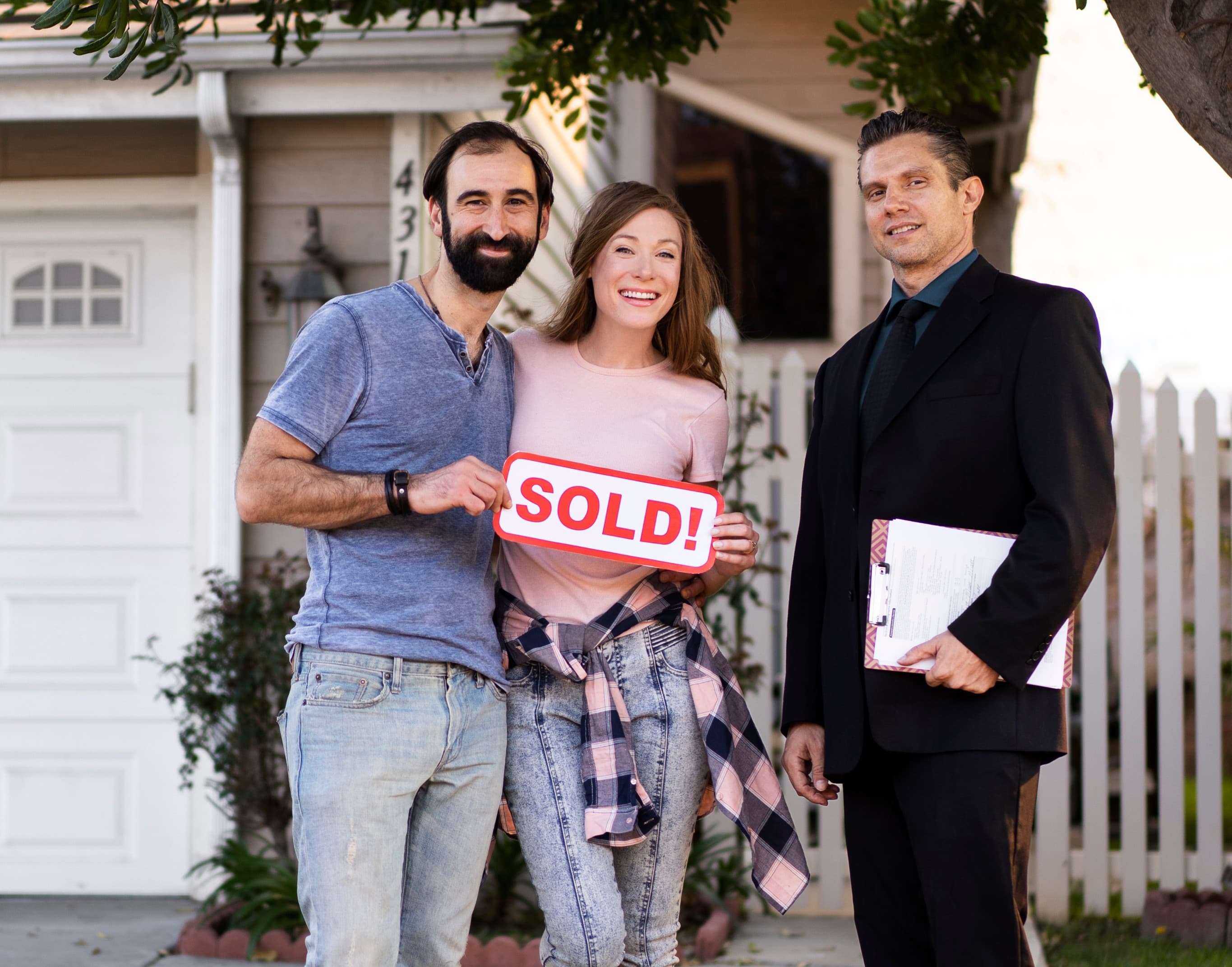 Couple proudly holding a SOLD sign with their real estate agent